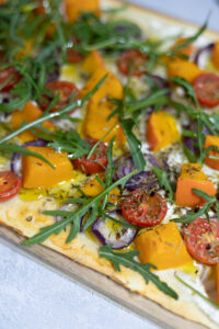 Flammkuchen belegt mit Rucola, mediterranen Kräutern, Süßkartoffel und Tomaten